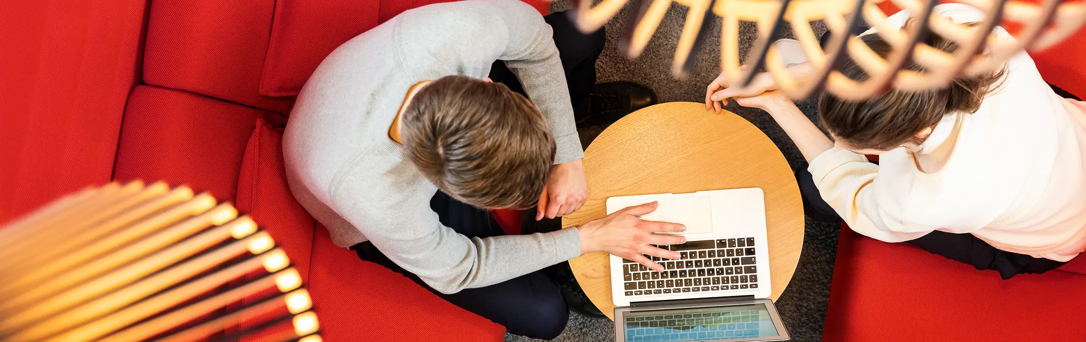 Two people sitting on a red sofa and working together on a laptop