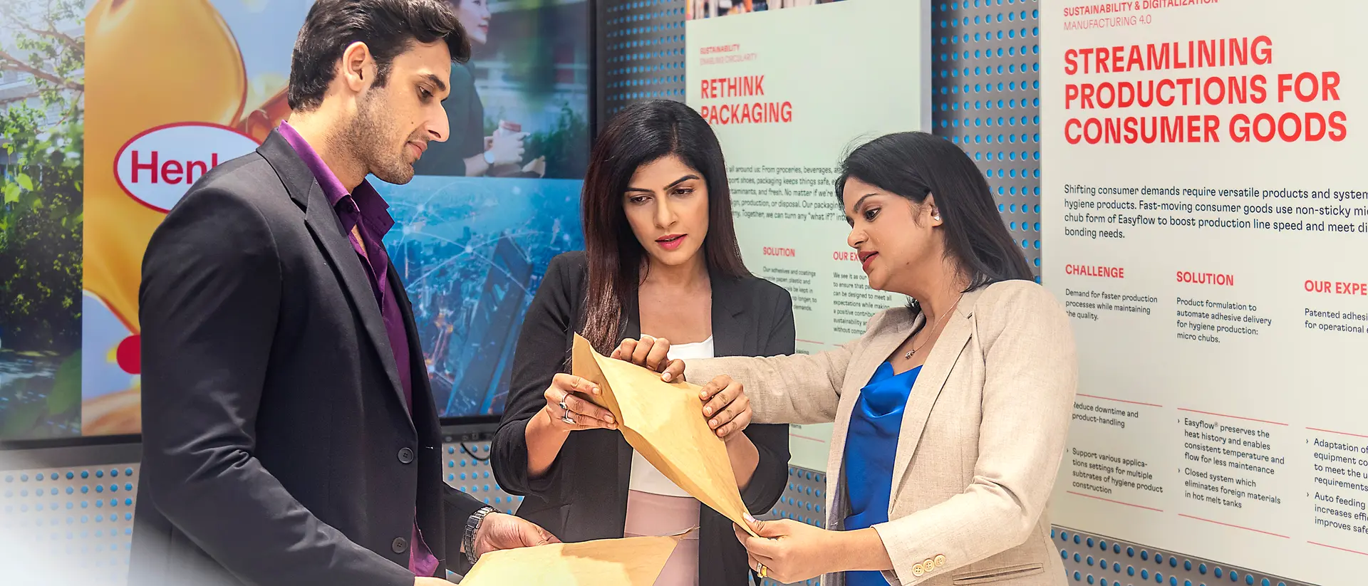 A customer experience tour guide presents application examples from Henkel Adhesive Technologies to two customers at the Technology Center Mumbai.