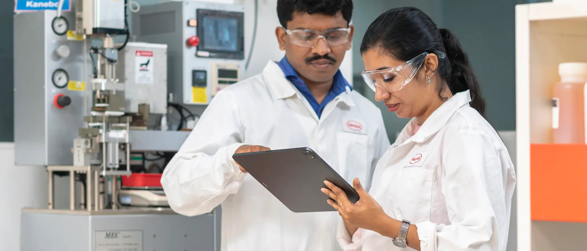 Two lab staff in lab coats discuss a test using a tablet in a laboratory at the Technology Center Mumbai development center.